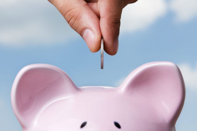 a person putting a coin into a pink piggy bank.